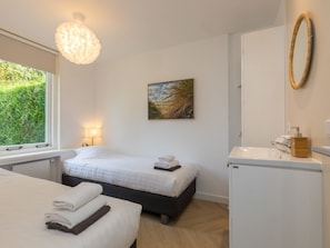Ein Hotelzimmer mit Bett, Nachttisch, Lampe und Blick auf Grünfläche.