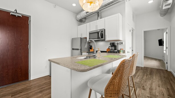 A modern kitchen with white cabinets, stainless steel appliances, and a bar area with wicker chairs. - 1 BR King Suite - Freshwater Inn - Bridgman, MI (Bridgman)