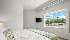 A bedroom with a bed, a TV, a window with a view of a parking lot and a building. - 1 BR King Suite - Freshwater Inn - Bridgman, MI (Bridgman)