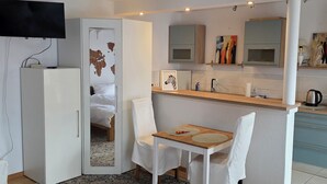 A compact hotel room with a bed, a desk with a chair, a kitchenette, and a TV mounted on the wall. - Cozy vacation apartment in HD-Wieblingen (Heidelberg)