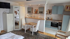 A compact hotel room with a bed, a small dining table with chairs, a kitchenette, and a TV mounted on the wall. - Cozy vacation apartment in HD-Wieblingen (Heidelberg)