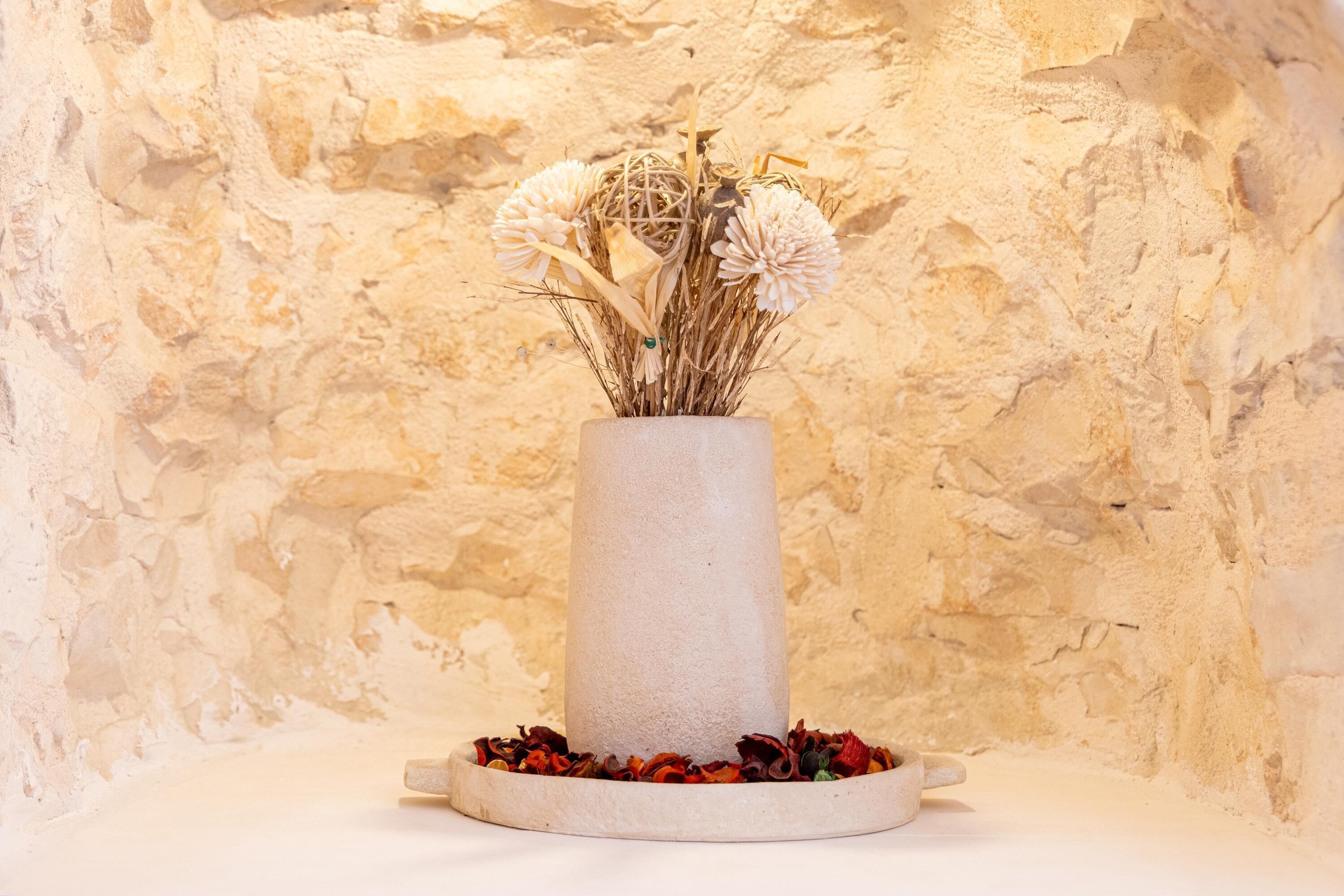 Eine Vase mit getrockneten Blumen und Zweigen vor einer strukturierten Wand.