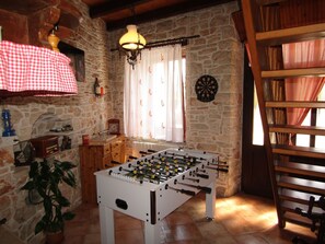 A room with a foosball table, a dartboard, a window with curtains, a wooden bench, and a stone wall. - House Batel by Interhome (Barbariga)
