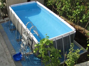 A rectangular swimming pool with a ladder on one side, surrounded by a garden with green plants. - House Batel by Interhome (Barbariga)