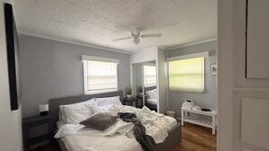 Een slaapkamer met een bed, nachtkastjes, een ventilator in het plafond en een raam met jaloezieën.