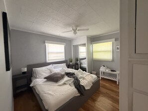 A bedroom with a bed, bedside tables, a nightstand, a ceiling fan, and a window with blinds. - Sleeps 16! - Breaking Away to Bloomington (Bloomington)