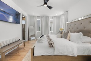 Ein modernes Schlafzimmer mit einem großen Bett, einem Deckenventilator und Blick ins Freie.