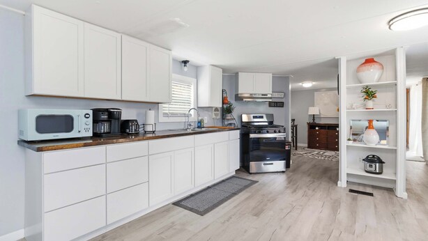 A modern kitchen with white cabinets, a microwave, a coffee maker, and a stove.