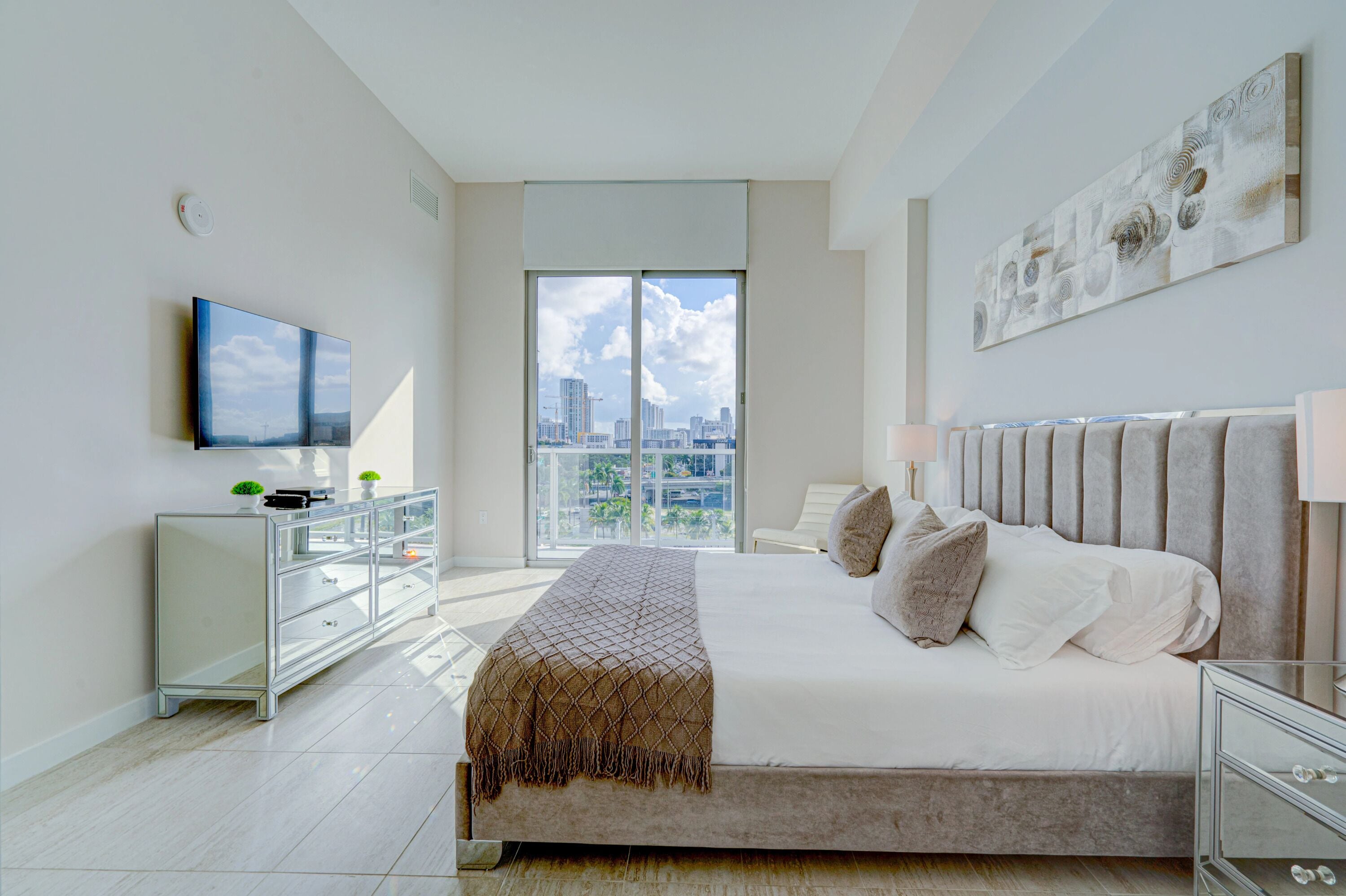 Ein modernes Schlafzimmer mit einem großen Bett, einem Fernseher, Blick auf die Stadt und einem minimalistischen Design.