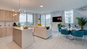 A modern kitchen with a central island, a dining area with teal chairs, and a TV mounted on the wall. - AEA - Biscayne BLVD Miami (Miami)