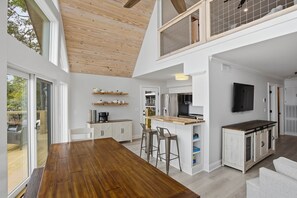 A modern kitchen with white cabinets, a wooden ceiling, and a dining area with a large table and bar stools. - Brighter Days-Lake Martin Retreat (Tallapoosa County)