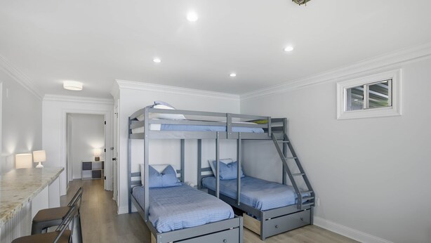 Ein Zimmer mit Etagenbetten, einem Schreibtisch mit Hocker, einer kleinen Küche und einem Fenster.