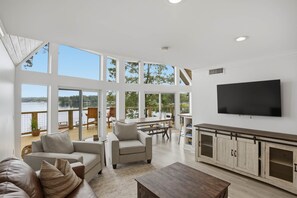 A spacious living area with large windows, a flat-screen TV, and a wooden dining table. - Brighter Days-Lake Martin Retreat (Tallapoosa County)