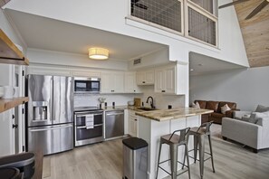 Een moderne keuken met roestvrijstalen apparatuur, een houten kookeiland en een hoge plafond met een houten balk.