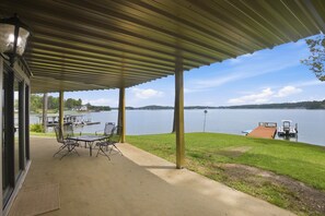 Une terrasse couverte avec une table et des chaises, une vue sur un lac et un quai avec un bateau.