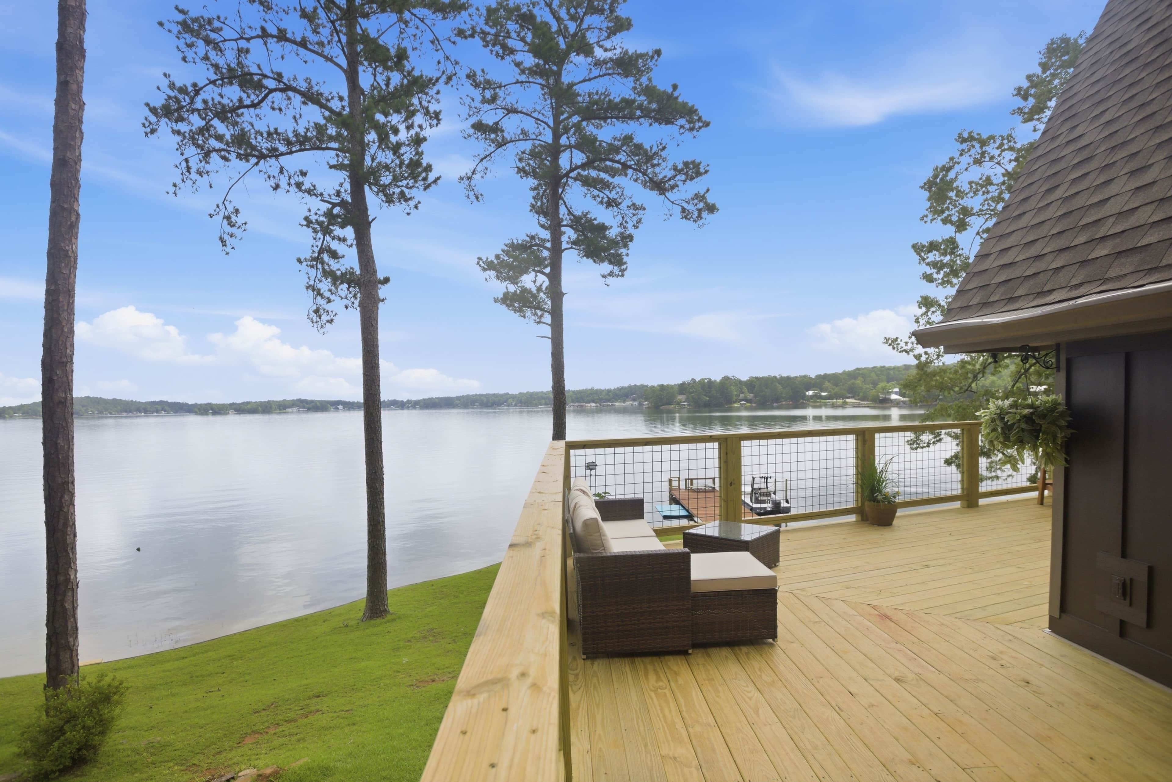 A deck with outdoor furniture overlooking a lake, surrounded by trees.