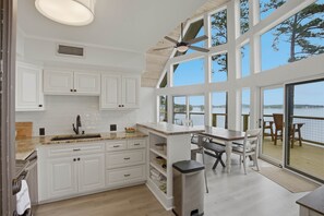 A kitchen with white cabinets, a granite countertop, and a view of the outdoors through large windows. - Brighter Days-Lake Martin Retreat (Tallapoosa County)