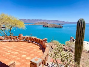 A patio with a tiled floor, a cactus, and a view of a turquoise lake with boats.