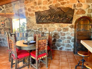 Una habitación con paredes de piedra, una mesa redonda, sillas y un mural.
