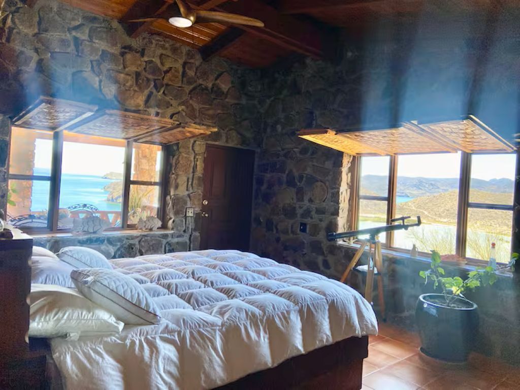 Une chambre avec des murs en pierre, un grand lit et une vue sur le paysage par les fenêtres.