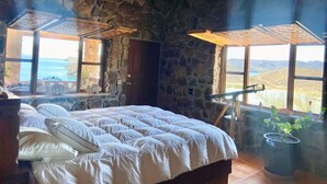 Un dormitori amb parets de pedra, un llit gran i vista al paisatge a través de les finestres.