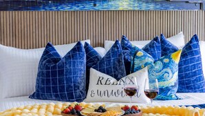 A bed with a white quilt, blue pillows, a plate of snacks, and a wine glass.