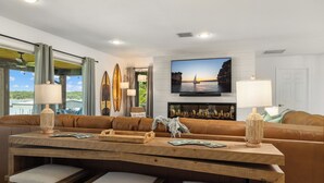 A modern living room with a wooden dining table, leather sofa, and a television displaying a sunset view.