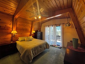 A wooden cabin bedroom with a bed, two bedside lamps, a ceiling fan, and a view of the outdoors through a window. - Chalet Getaway in Beautiful Show Low Arizona (Show Low)