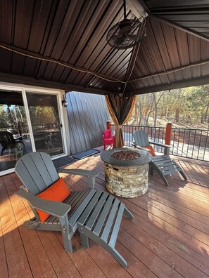 Une terrasse couverte avec des fauteuils Adirondack, un foyer et une porte vitrée donnant sur un espace extérieur.