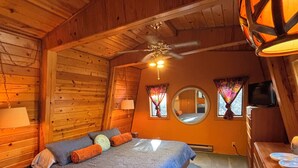 Un dormitorio acogedor con techo de madera, cama con ropa de cama azul, un espejo redondo y un ventilador de techo.