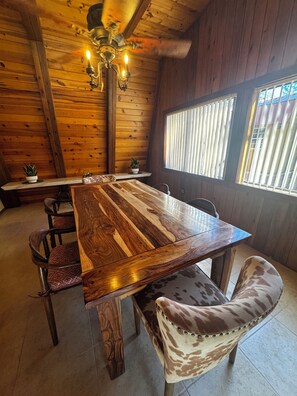 Une table Ă manger en bois, des chaises, un lustre et une fenĂȘtre avec des stores.