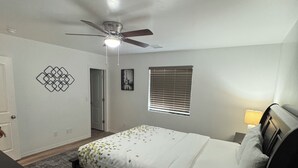 Ein Schlafzimmer mit einem Bett, einem Deckenventilator, einem Fenster mit Jalousien, einer Tür und einer Wanddekoration.