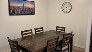 Ein Esszimmer mit Holztisch und -stühlen, einem Stadtbildgemälde, einer Uhr und einer Deckenleuchte.
