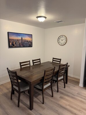 Ein Esszimmer mit Holztisch und -stühlen, einem Stadtbildgemälde, einer Uhr und einer Deckenleuchte.