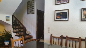 Ein Essbereich mit einem Glastisch, Holzsesseln, einer Treppe und einer Wand mit gerahmten Bildern.