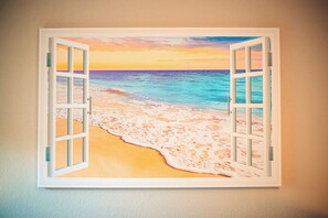 Ein Fenster mit Blick auf Strand und Meer bei Sonnenuntergang.