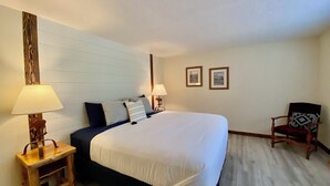 A hotel room with a large bed, two bedside lamps, a wooden chair, and two framed pictures on the wall. - Lazy Lake Outpost (Kettle Falls)