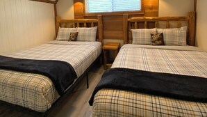 A room with two beds, a ceiling fan, a window with blinds, and a small table. - Lazy Lake Outpost (Kettle Falls)
