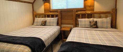 A room with two beds, a ceiling fan, a window with blinds, and a small table.