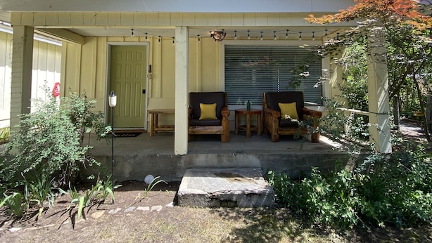 A house with a gabled roof, a porch with wooden furniture, and a garage door. - Lazy Lake Outpost (Kettle Falls)
