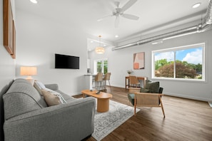 Una sala de estar moderna con un sofá gris, una mesa de centro de madera y un comedor con sillas y una mesa.