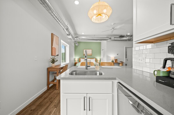 Una cocina moderna con una isla central, muebles blancos y una lámpara colgante.