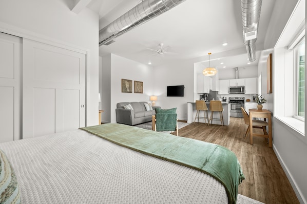 Un dormitorio moderno con una cama grande, un sofá, una zona de comedor y una cocina.