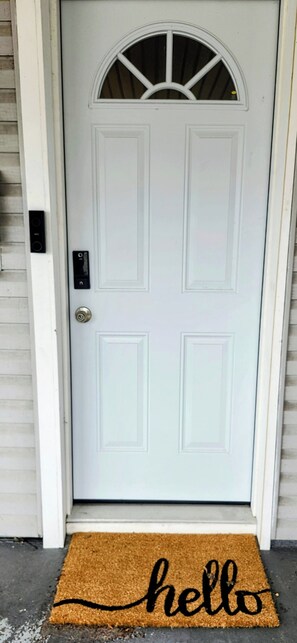 A white door with a small window, a doorbell, and a doormat with 'hello' written on it.