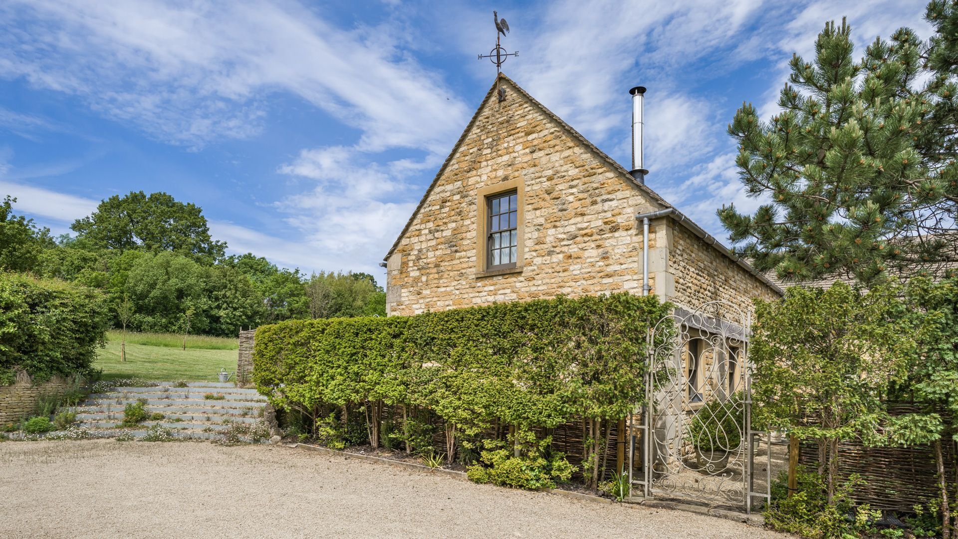 Une maison en pierre avec un toit triangulaire, une cheminée et un portail en métal.