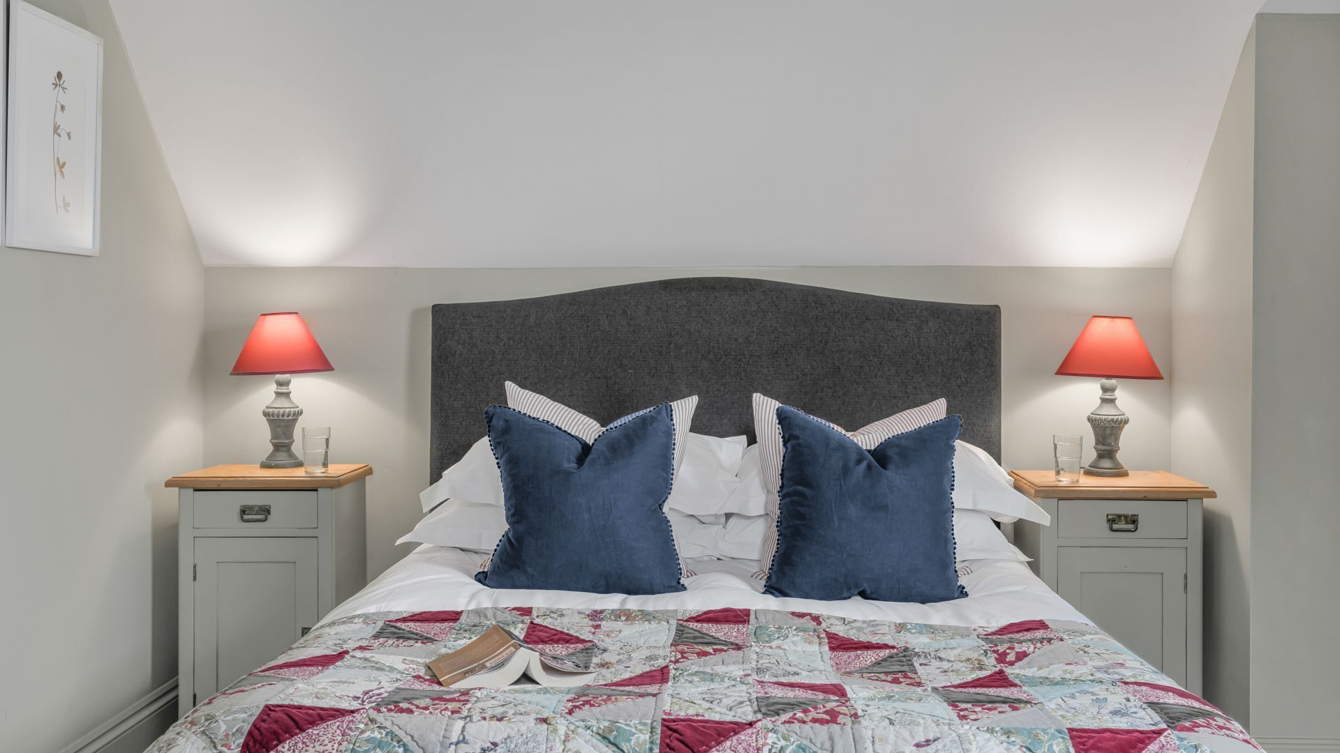 Un letto rifatto con copria letto e due comodini con lampade, e una testiera.