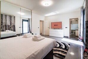 Ein modernes Hotelzimmer mit einem großen Bett, einem Fernseher, einem Spiegel und einem durch eine offene Tür einsehbaren Badezimmer.