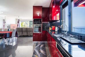 Eine moderne Küche mit Edelstahlgeräten, ein Essbereich mit Tisch und Stühlen sowie Meerblick durch große Fenster.