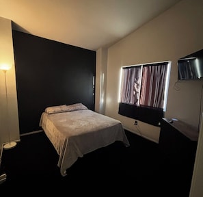 Ein Schlafzimmer mit einem Bett, einem Fernseher, einer Lampe und einem Fenster mit Vorhängen.