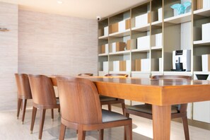 A dining area with a wooden table and chairs, a coffee machine, and a bookshelf with various items. - Ji Hotel (Nanjing)